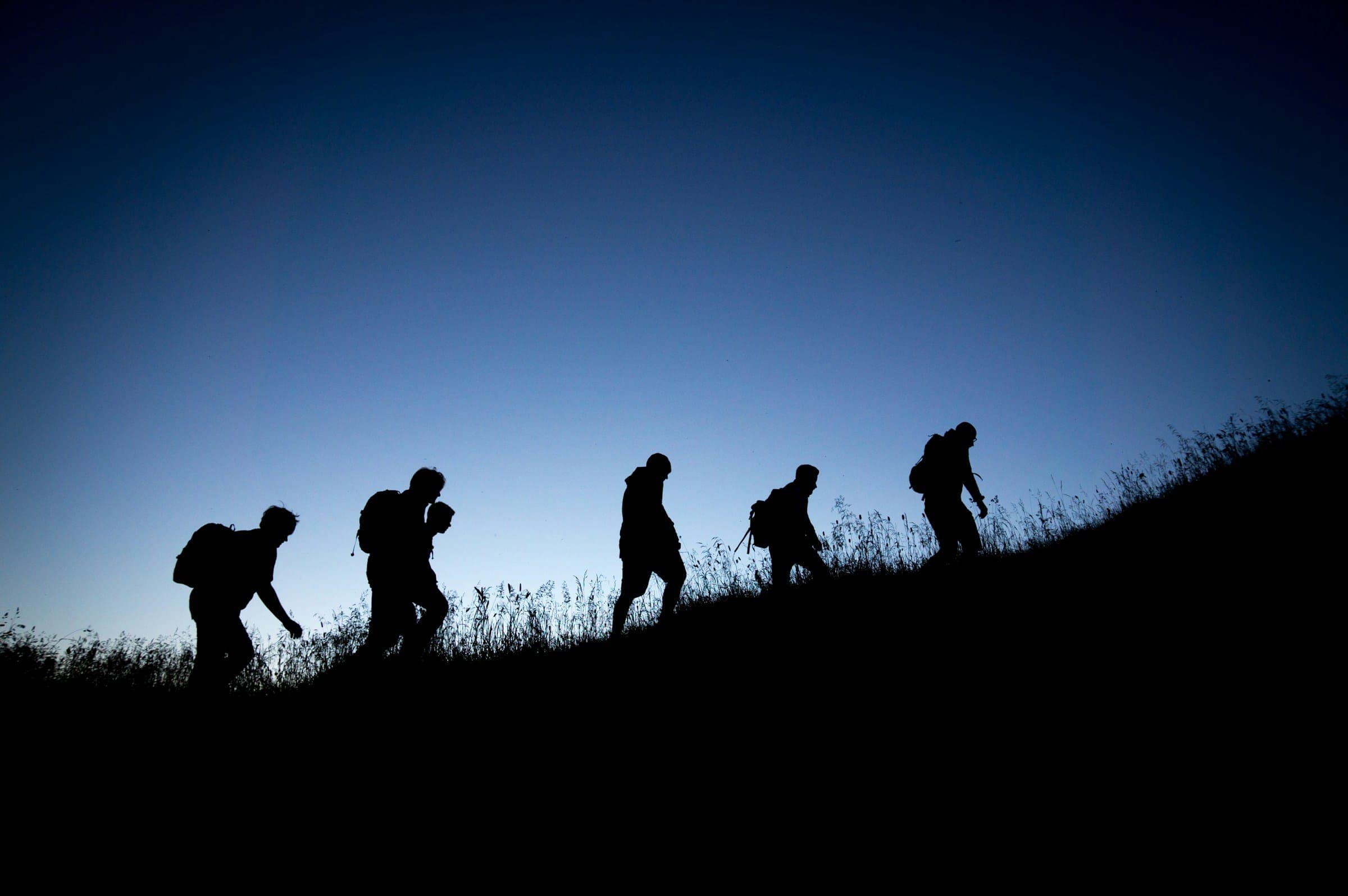 Groep wandelaars met rugzakken als silhouet op een heuvel
